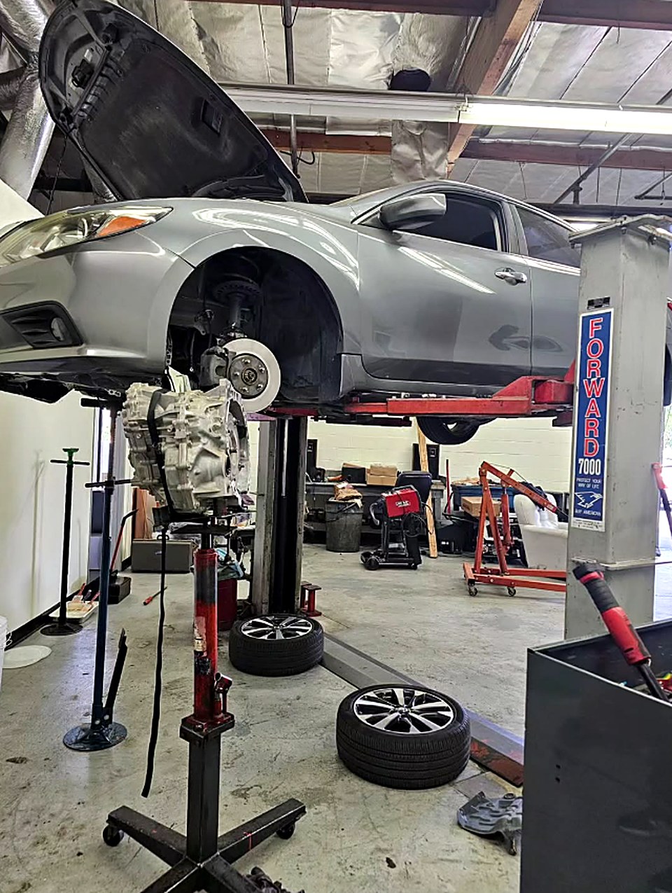 Inside GMR Elite Auto: a sedan raised on the lift with its hood open and a transmission on a jack stand below